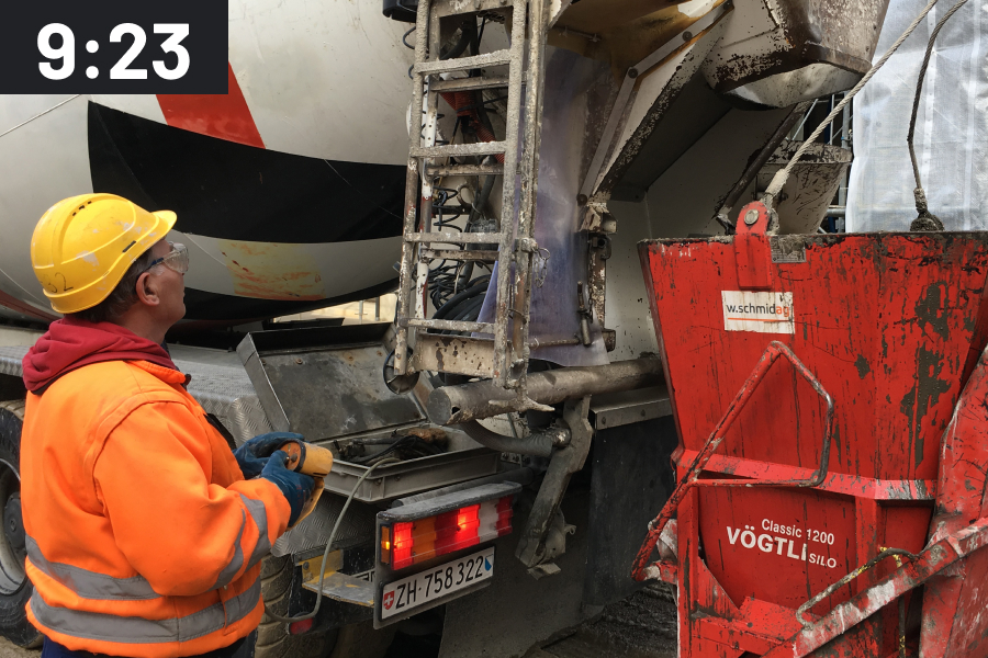 Unloading a concrete mixer truck into a red shipping container at the construction site with a time stamp of 9:23 a.m.