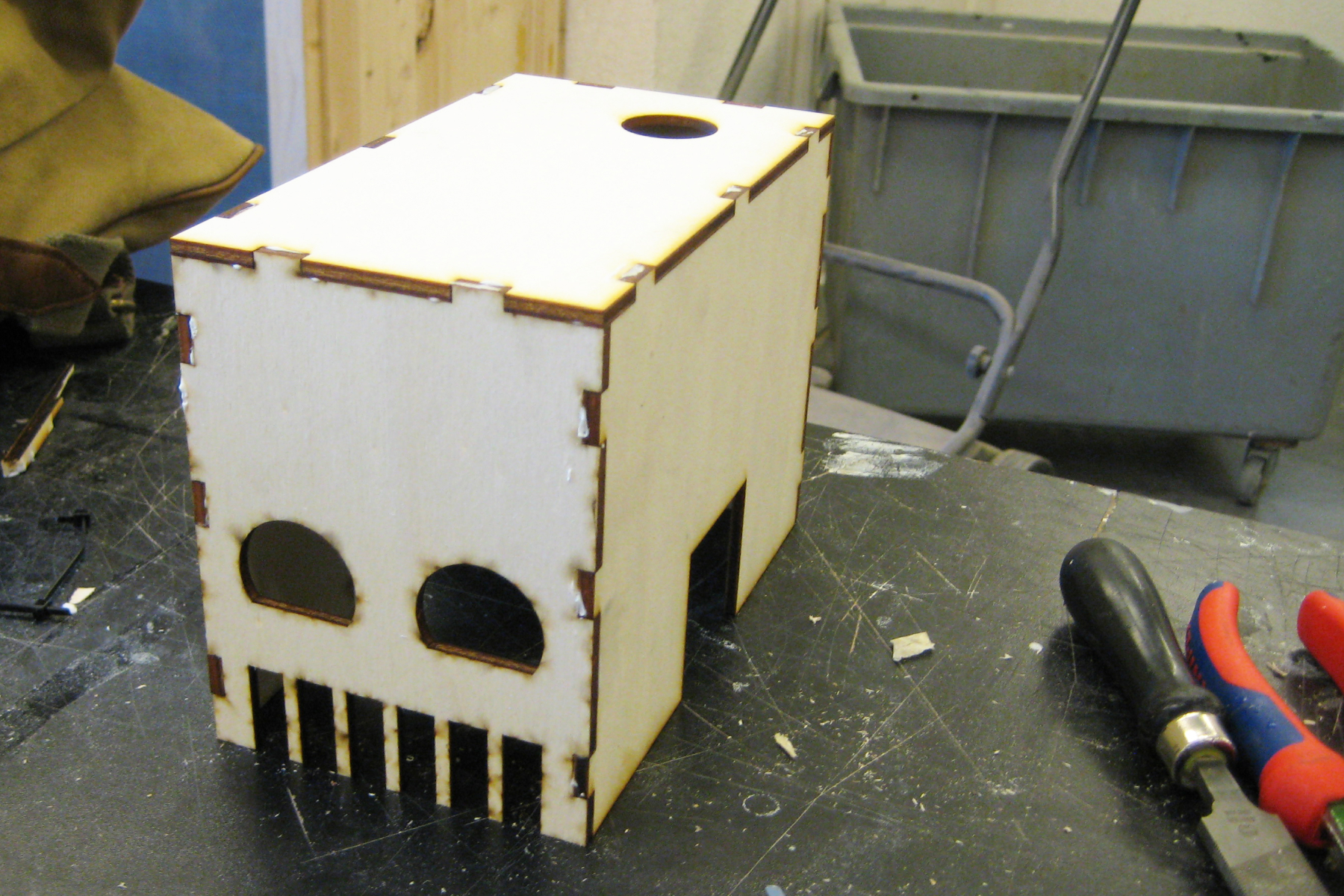 A laser-cut wooden housing for the robot on a work table with tools.