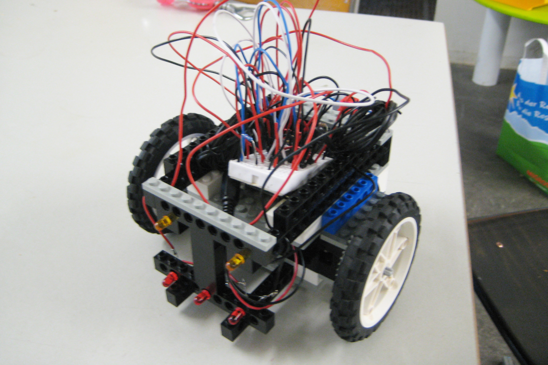 A self-built two-wheeled robot from Lego elements with a complex cable structure and LEDs on the front.