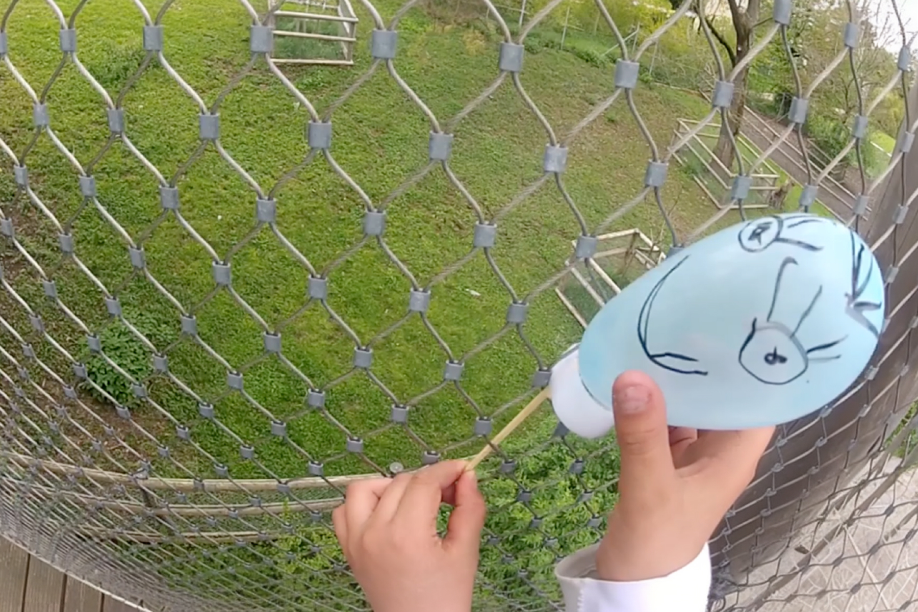 Perspective of a child holding a self-painted balloon near a large wire fence.